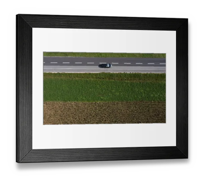 Framed Print : Drone view of a country road with a car between harvested fields