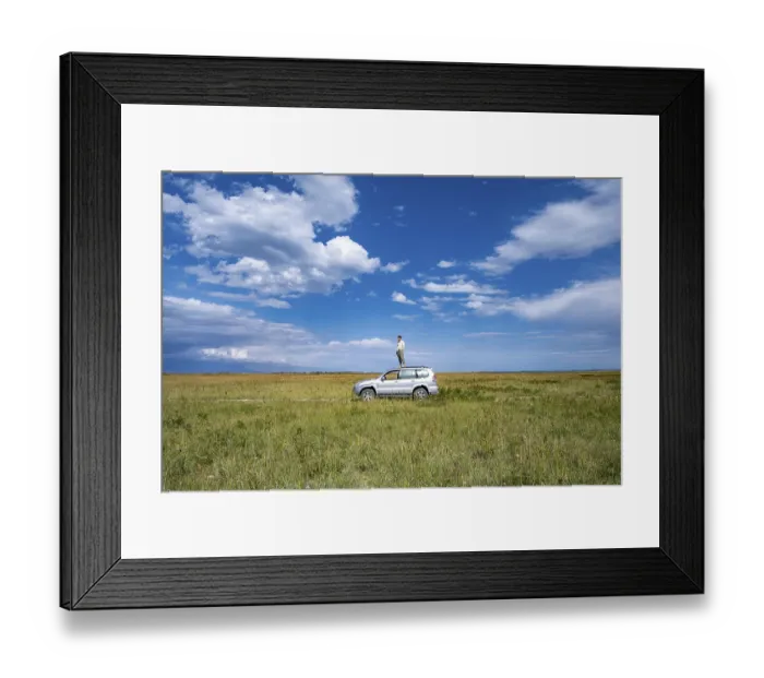 Framed Print : A man stands on a car in the centre of a vast landscape under a blue sky
