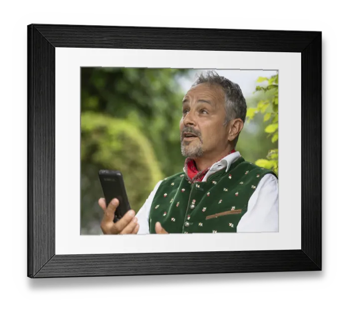 Framed Print : Man in Bavarian traditional traditional costume with mobile phone in hand looks astonished Framed Print : Man in Bavarian traditional traditional costume with mobile phone in hand looks astonished