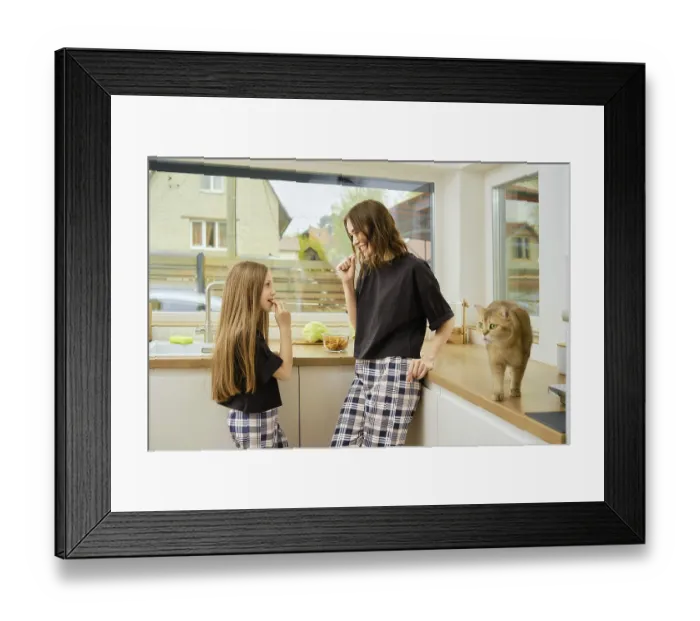 Framed Print : Playful mother and daughter bite crackers looking at each other while standing in bright kitchen