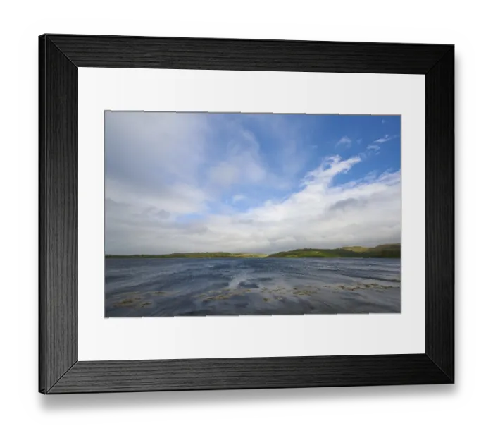 Framed Print : A lake with blue sky and clouds surrounded by green hills