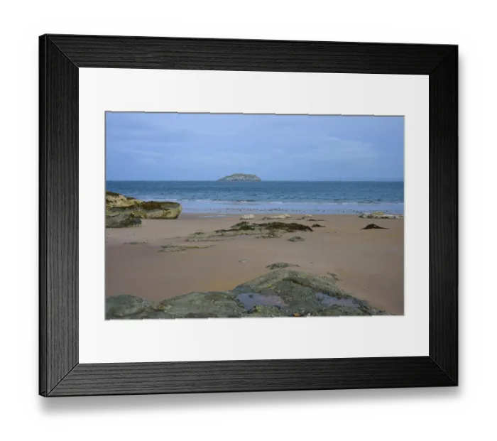 Framed Print : Sandy beach beach with rocks and distant island under cloudy sky