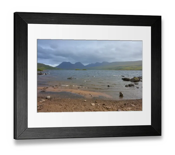 Framed Print : Shores of a lake with waves and mountains in the background under cloudy sky