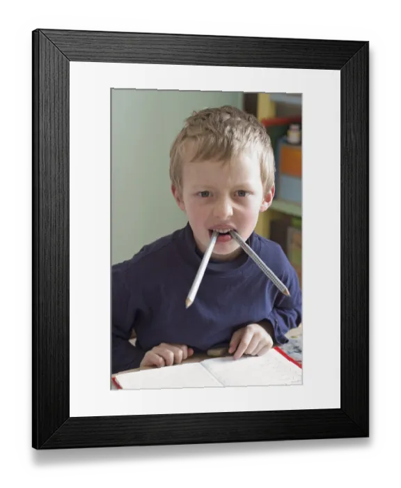 Framed Print : Six year old boy sitting at desk doing homework