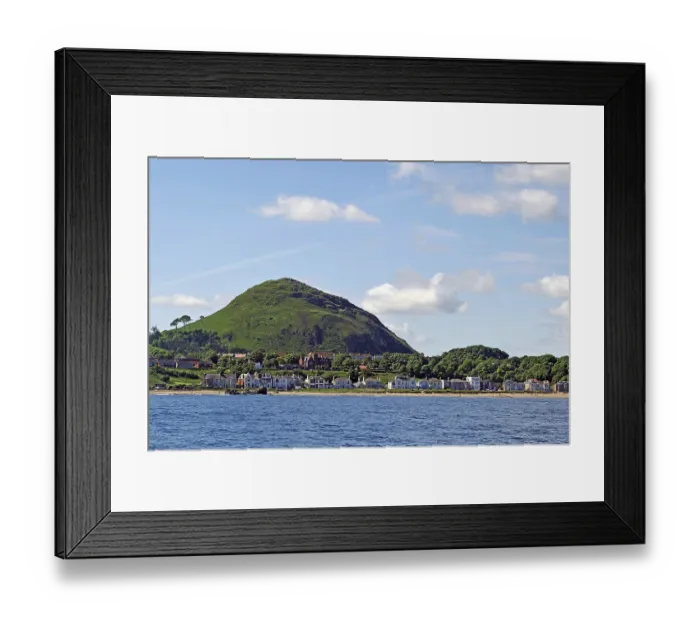 Framed Print : Coastal town with houses and a green hill in the background by the sea