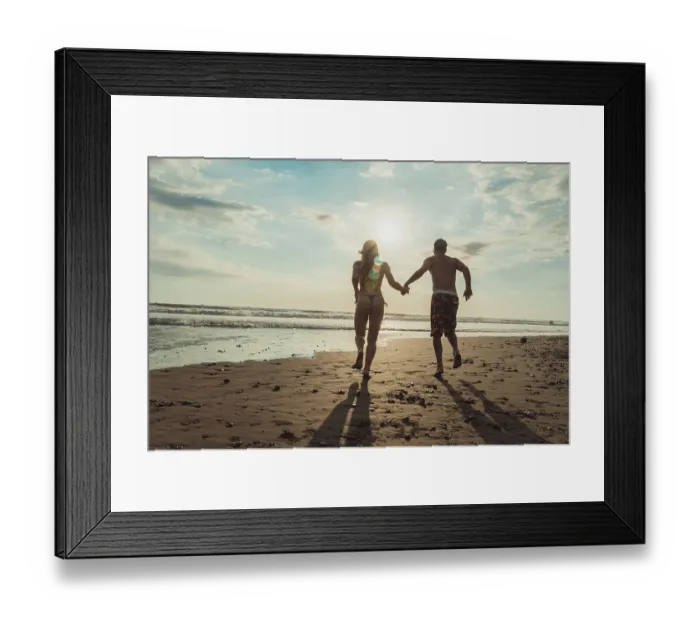 Framed Print : Rear view of couple running hand in hand along a sandy beach at sunset