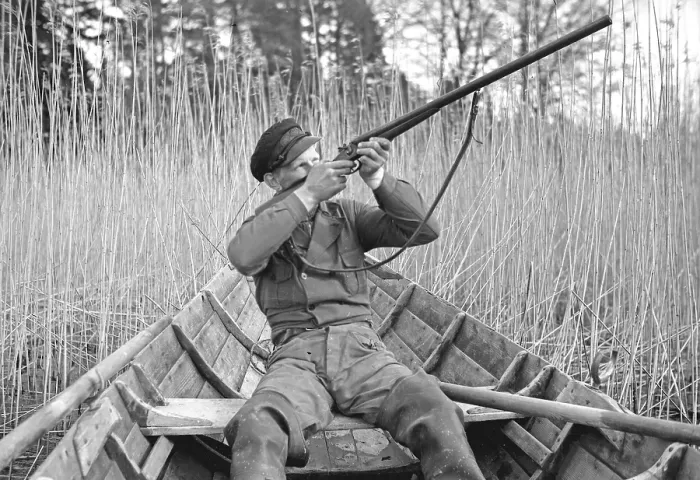 Framed Print : In the 1930s. A man sits in a rowing boat and aims his rifle upwards to shoot ducks Framed Print : In the 1930s. A man sits in a rowing boat and aims his rifle upwards to shoot ducks