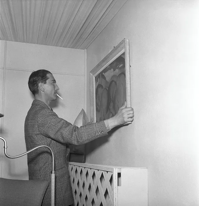 Framed Print : In the 1940s. A man tries to put a painting up on the wall and is carefully adjusting it so it hangs right Framed Print : In the 1940s. A man tries to put a painting up on the wall and is carefully adjusting it so it hangs right