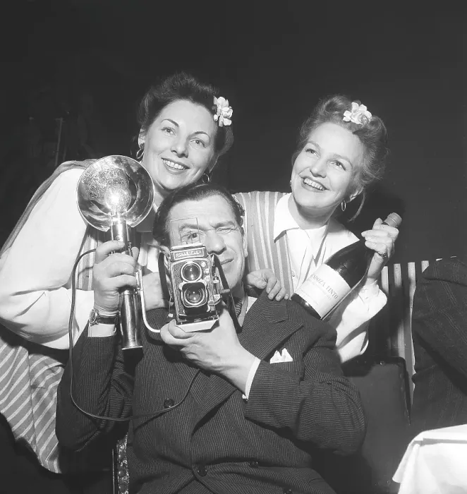 Framed Print : 1940s photographer. A man with a Rolleiflex camera and flash aims at something with two girls haning on his shoulders