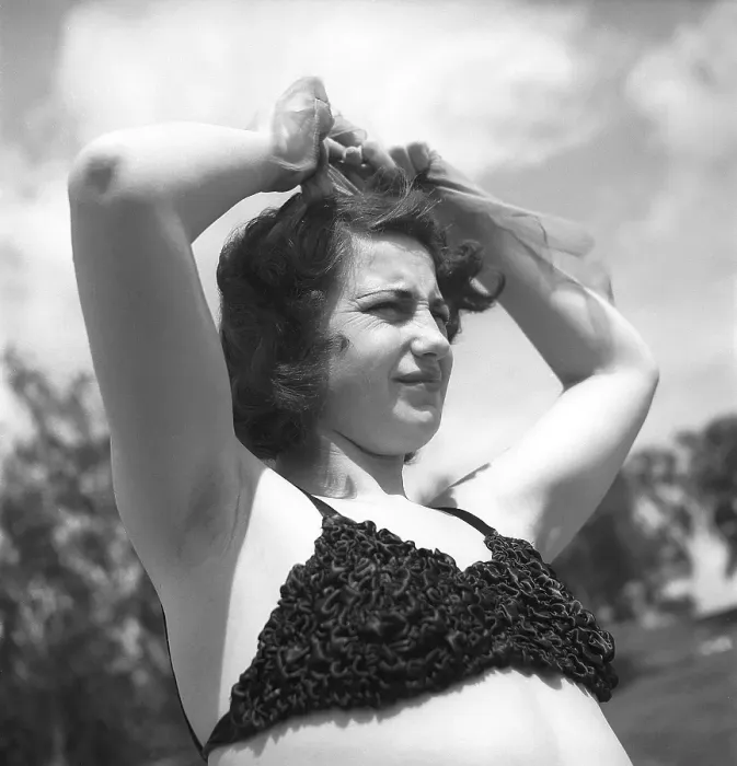 Framed Print : 1940s summer. A young woman in a bikini top looks to be struggling with her hairdo Framed Print : 1940s summer. A young woman in a bikini top looks to be struggling with her hairdo