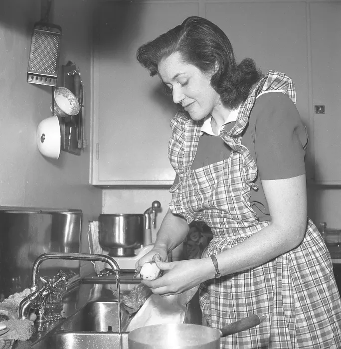Framed Print : In the 1940s. A woman in a typical 1940s kitchen with the details of the interior and the objects being very representative of the decade
