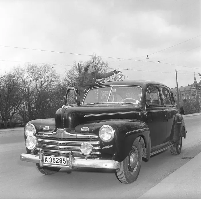 Framed Print : In the 1940s. A young woman by her passenger car of the American car brand Ford. She is dressed in a two-piece suit, skirt and short jacket in herringbone wool fabric Framed Print : In the 1940s. A young woman by her passenger car of the American car brand Ford. She is dressed in a two-piece suit, skirt and short jacket in herringbone wool fabric