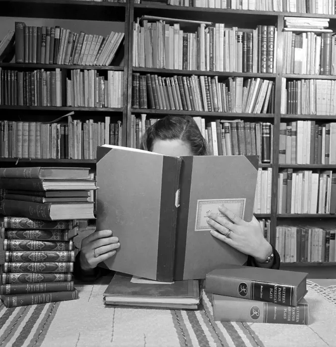 Framed Print : In the 1940s. A young woman in a room with bookshelves, has her face hidden behind the book she is reading. 1948 Kristoffersson ref AH31-8