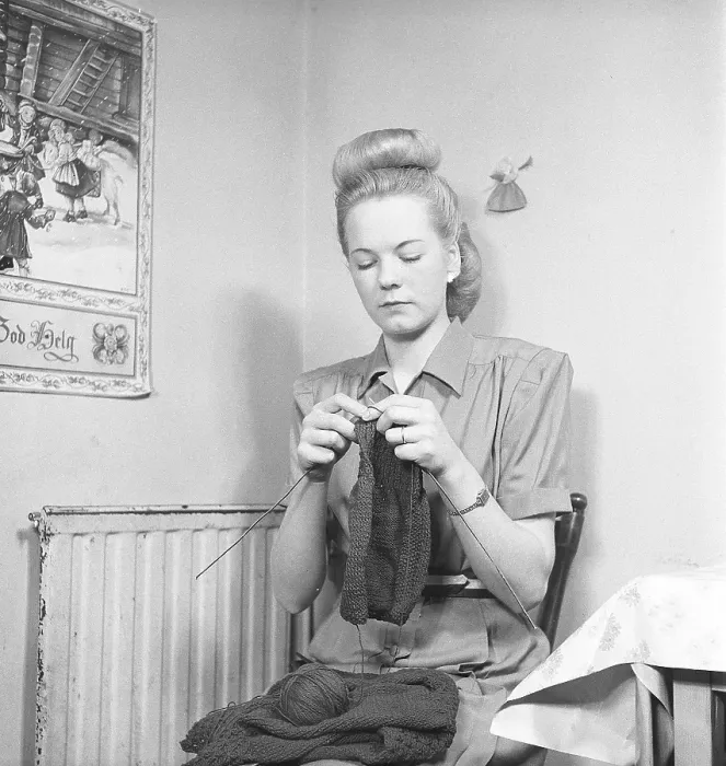 Framed Print : In the 1940s. A young woman sits in the kitchen on a chair and knits a sweater