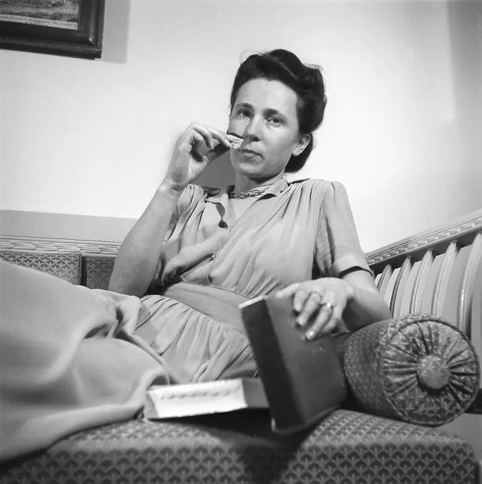 Framed Print : In the 1940s. A young woman is sitting on the couch with a piece of chocolate or candy in her hand from a box next to