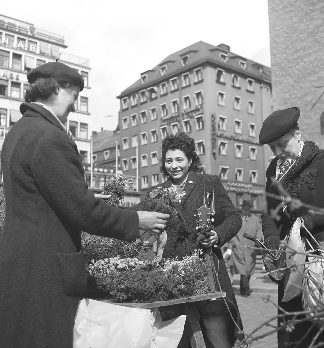 Framed Print : 1945 at Hoetorget in Stockholm Sweden. A lively scene at the outdoor flower market. Three women, dressed in mid-1940s coats and berets, engage in a cheerful exchange over a stall brimming with blooming plants and flowers