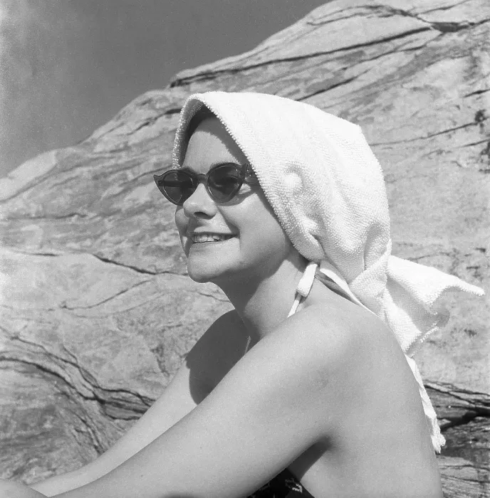 Framed Print : 1950s on the beach. A young woman on the beach takes extra care not to burn herself in the sun