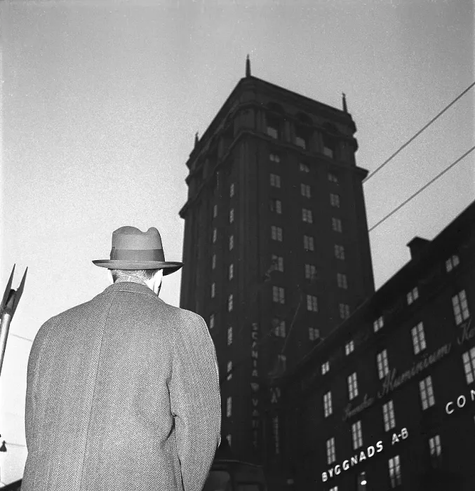 Framed Print : In the 1950s. A man in a coat and hat is pictured in the street from below with the silhouette of a high building in the background. Sweden 1951 Kristoffersson ref BE86-5