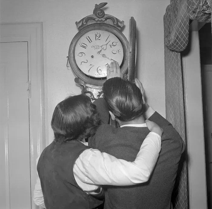 Framed Print : In the 1950s. A woman and a man in front of a antique clock with the clock-face visible