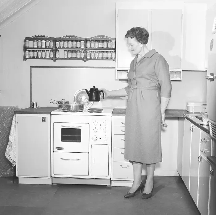 Framed Print : In the 1950s. A woman in a typical 1950s kitchen with wooden cabinets and a set of spices on shelfes above the cooker Framed Print : In the 1950s. A woman in a typical 1950s kitchen with wooden cabinets and a set of spices on shelfes above the cooker