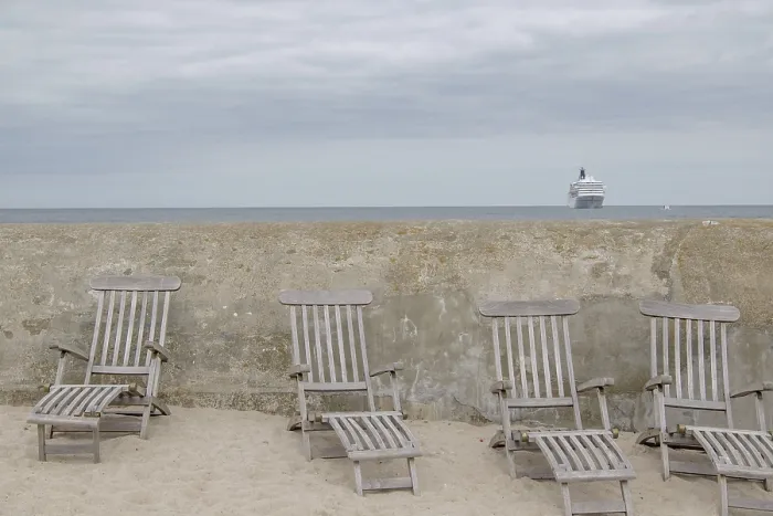 Framed Print : Abandoned deckchairs on the beach in front of a concrete wall with a cruise ship in the background