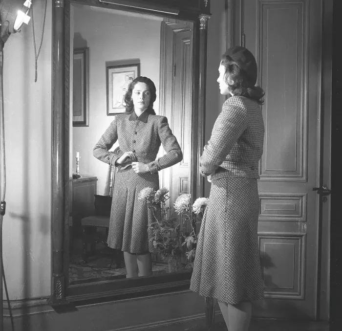 Framed Print : Actress Viveca Lindfors, 1920-1995. She stands in front of the mirror and buttons the last button of her plaid two-piece suit with a knee-length skirt and a waist-length jacket. 1945. Kristoffersson ref R55-6