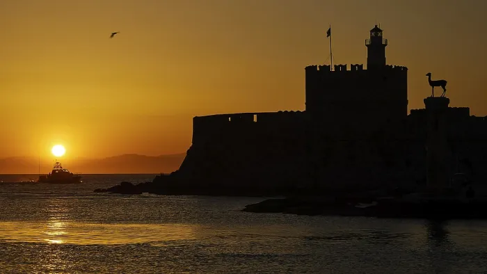 Framed Print : Agios Nikolaos fortress, sunrise over the sea with a castle silhouette and a passing boat