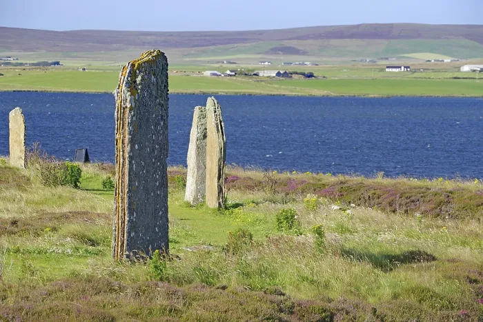 Framed Print : Ancient stones at the edge of a blue lake with green hills in the background