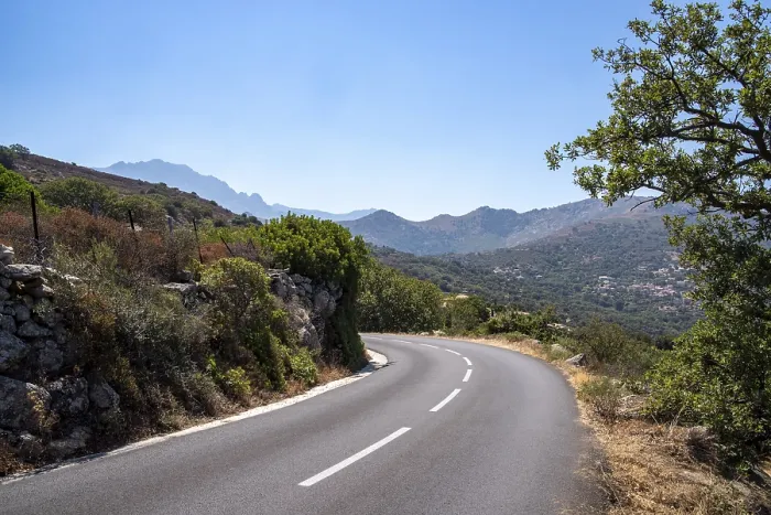 Framed Print : Empty asphalt road winding through green hills with distant mountains under a clear blue sky Framed Print : Empty asphalt road winding through green hills with distant mountains under a clear blue sky