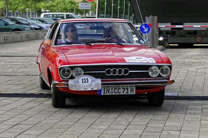 Framed Print : AUDI, A red vintage car drives on cobblestones with two people in the car