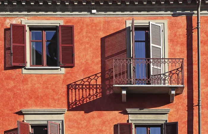 Framed Print : Balcony and wooden shutters on windows cast shadows on facade of the house with red wall on sunny day in town of Alba