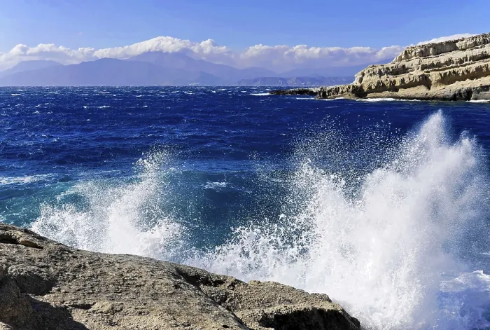 Framed Print : Bay, Matala beach, spray of waves crashing on rocks under a bright blue sky