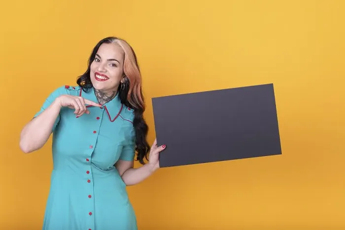 Framed Print : Beautiful woman pointing at a blank black board against a yellow background Framed Print : Beautiful woman pointing at a blank black board against a yellow background
