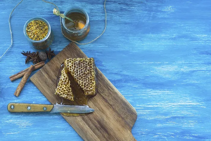 Framed Print : Bee pollens jar spices honeycomb piece with knife against blue textured background