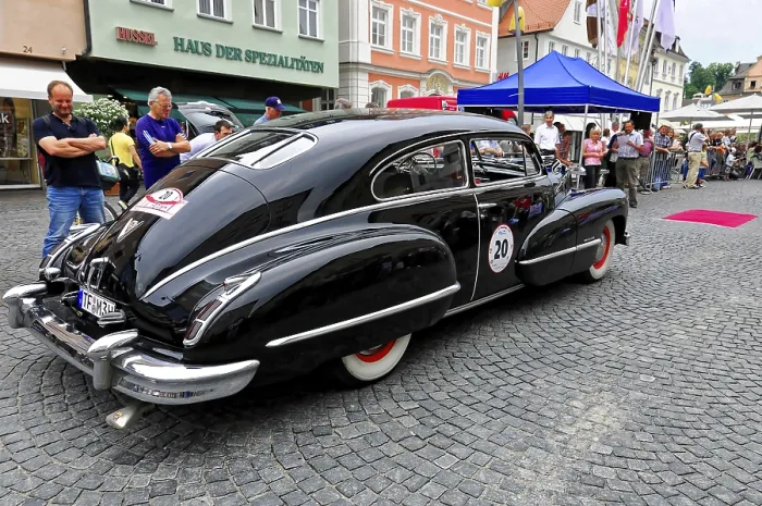 Framed Print : A black luxury classic car in front of a building surrounded by people