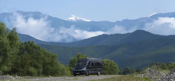 Framed Print : A black van on a road in a mountain valley with snowy peaks and clouds