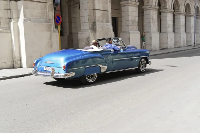 Framed Print : Blue convertible drives past a historic building