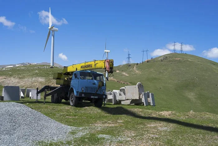 Framed Print : A blue crane lorry stands on a green construction site next to a wind turbine on a hill