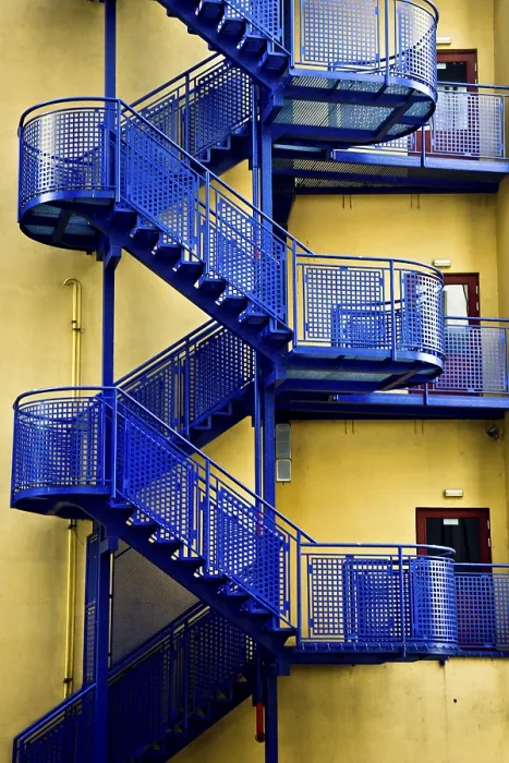 Framed Print : Blue metal fire escape staircases against a yellow wall creating a stark industrial contrast