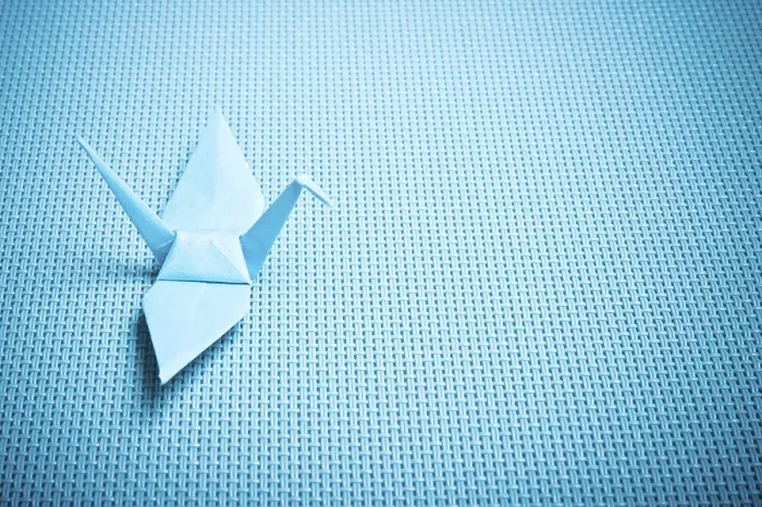 Framed Print : Blue origami crane resting on a woven textured surface Framed Print : Blue origami crane resting on a woven textured surface