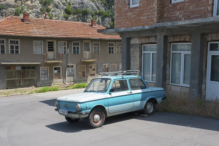 Framed Print : A blue retro car parked in front of dilapidated buildings under a clear sky