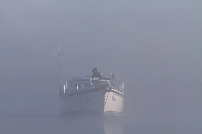Framed Print : A boat sails through misty water with wind turbines in the background