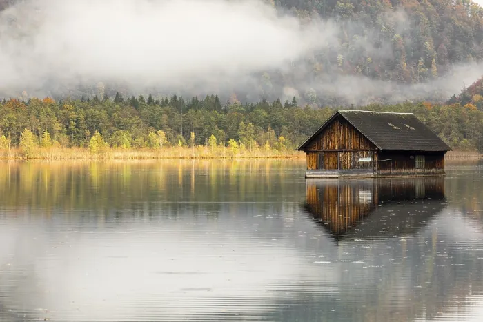 Framed Print : A boatshelter at lake Almsee. The forest in the background in full fall foliage and some fog above it