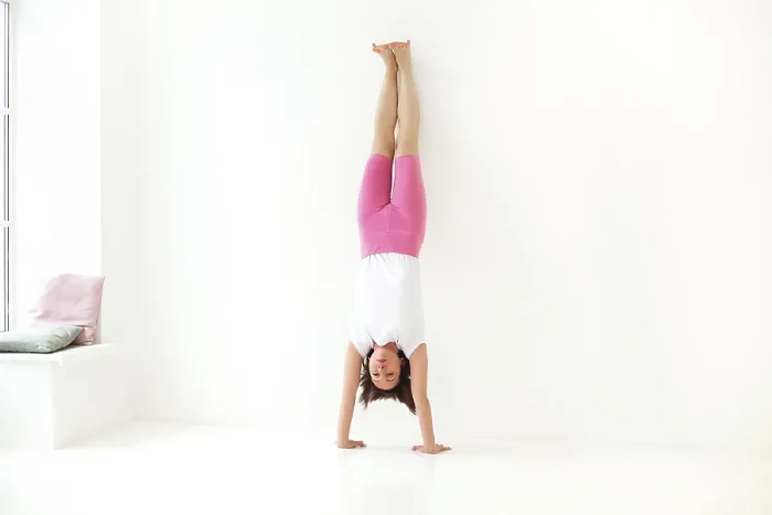 Framed Print : Full body of focused slim female female performing handstand near wall while practicing yoga in light room by