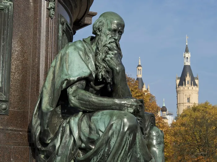 Framed Print : Bronze statue of a pensive man in front of a historic castle on an autumn day