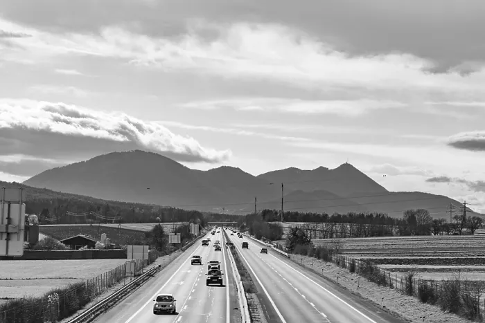 Framed Print : Busy motorway in front of a mountain backdrop in black and white with cloudy sky Framed Print : Busy motorway in front of a mountain backdrop in black and white with cloudy sky
