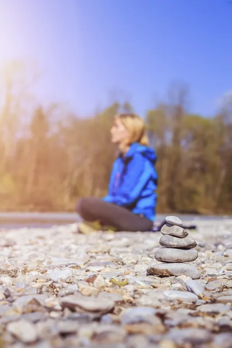 Framed Print : Cairn on a pebble beach, meditating woman in the background Framed Print : Cairn on a pebble beach, meditating woman in the background
