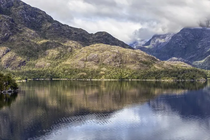 Framed Print : Calm ocean with clear reflection of forested mountains and cloudy skies in a peaceful setting Framed Print : Calm ocean with clear reflection of forested mountains and cloudy skies in a peaceful setting