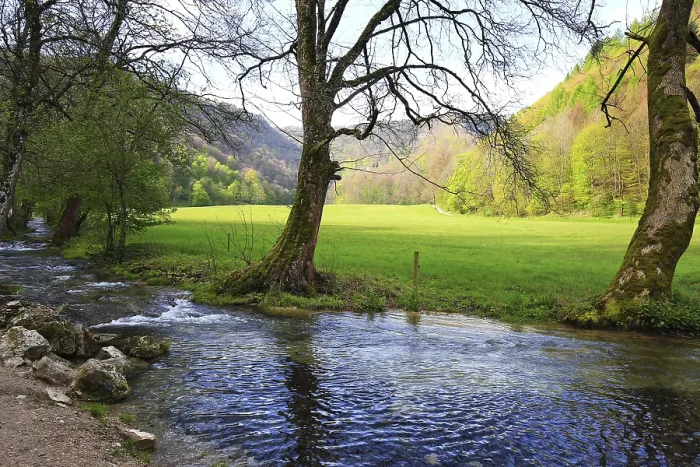 Framed Print : A calm river flows through a green meadow with wooded hills in the background