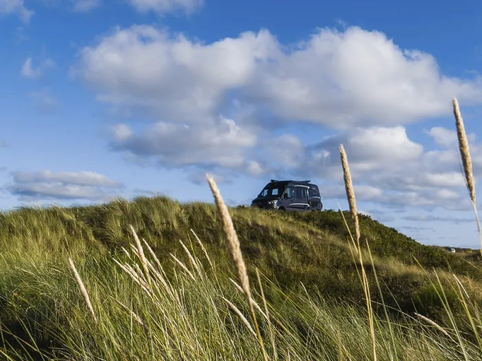 Framed Print : A campervan stands on a grassy dune under a blue sky with clouds